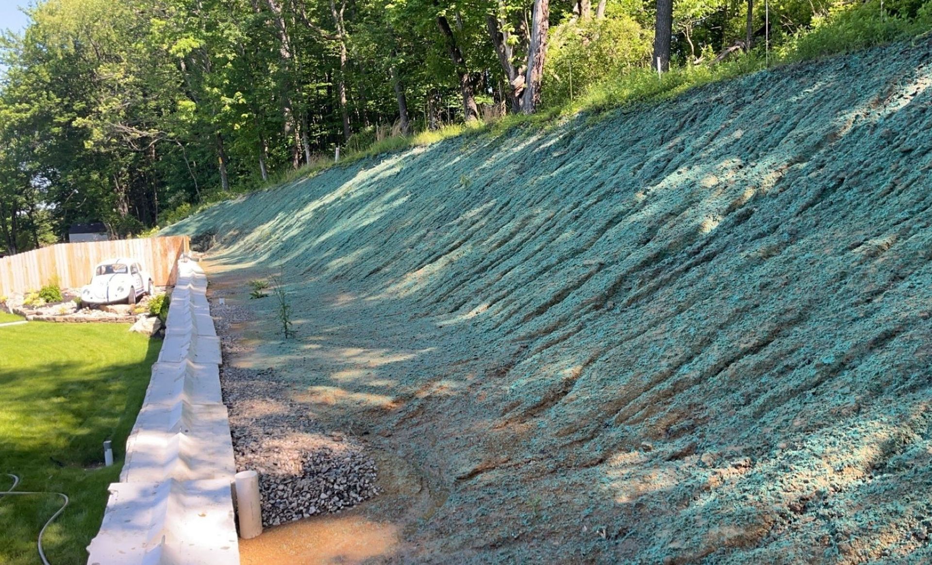 A steep hillside covered in green erosion control netting; a retaining wall and lawn are in the foreground.