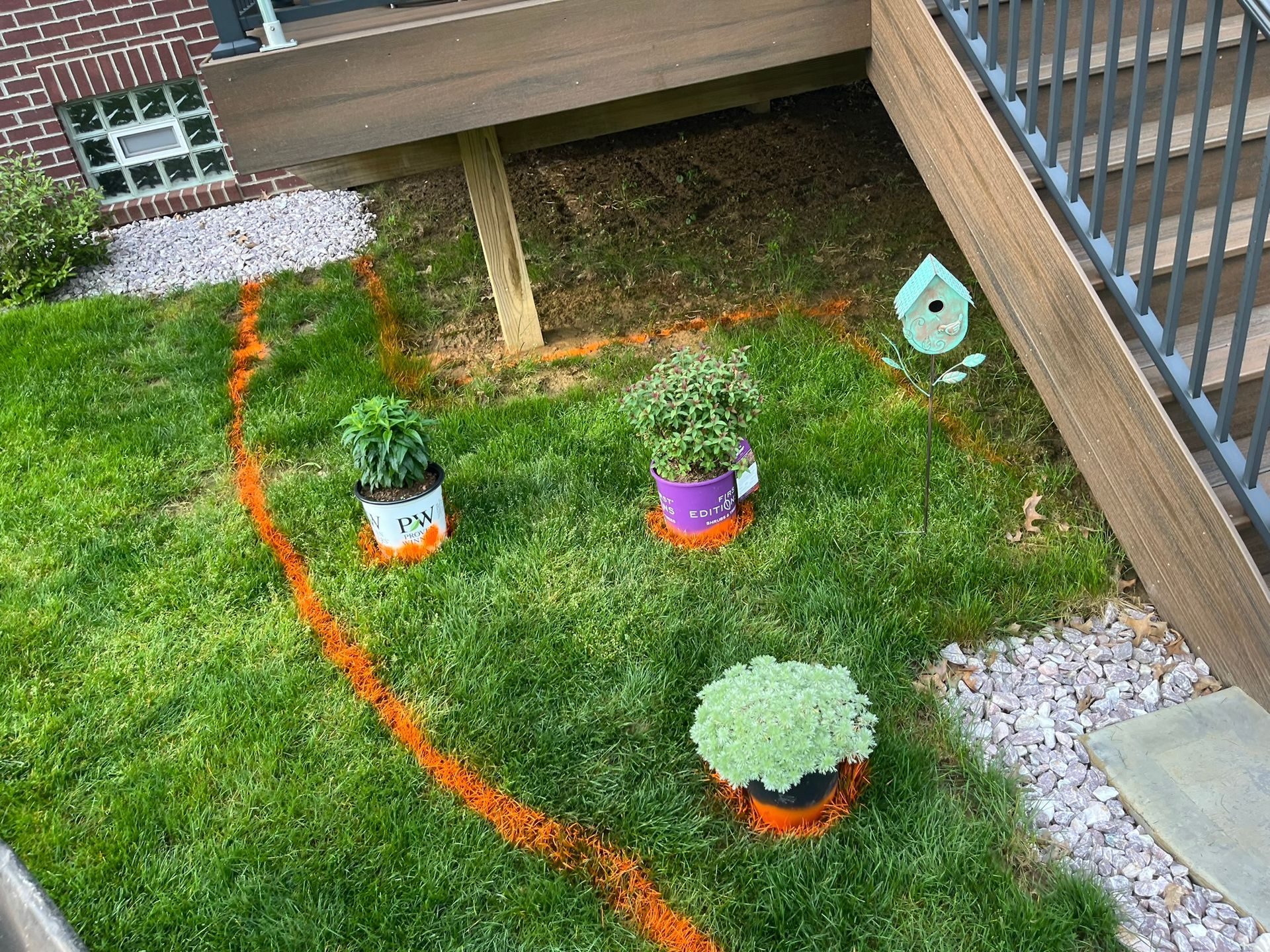 A small backyard garden area outlined in orange spray paint, with potted plants and a birdhouse.