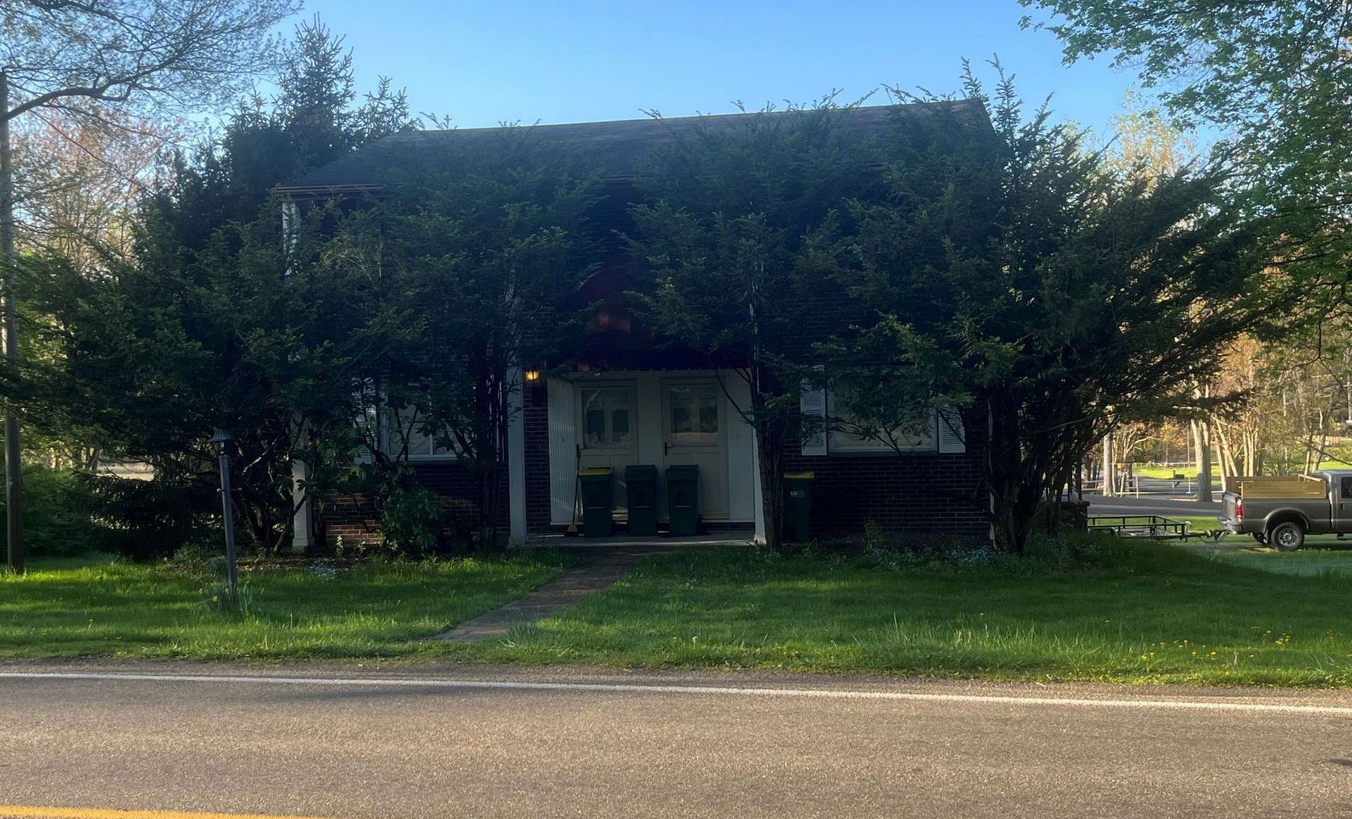A house partially obscured by green trees; road in foreground, car on right.