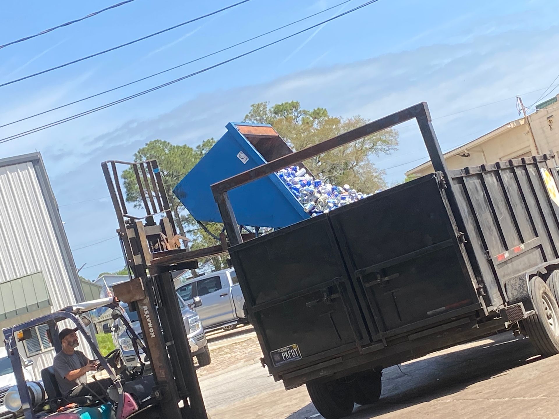 A forklift is loading a dumpster into a trailer.