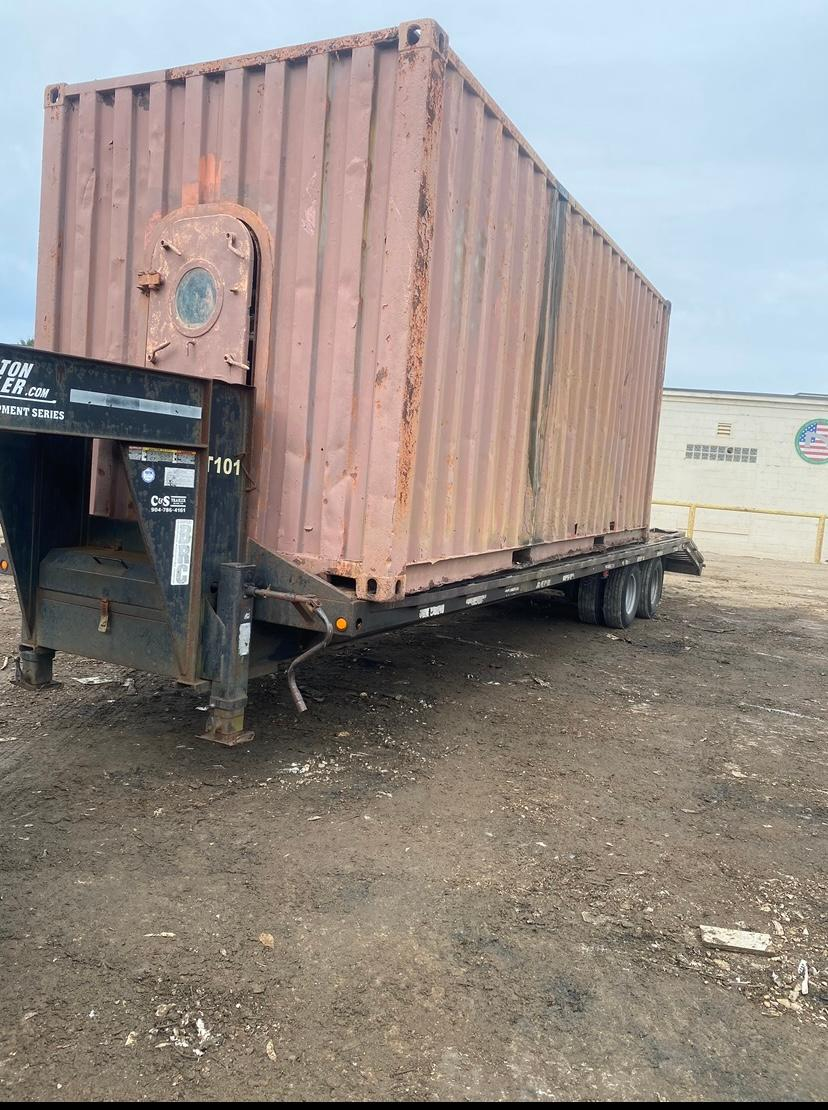 A shipping container is sitting on top of a trailer in a dirt field