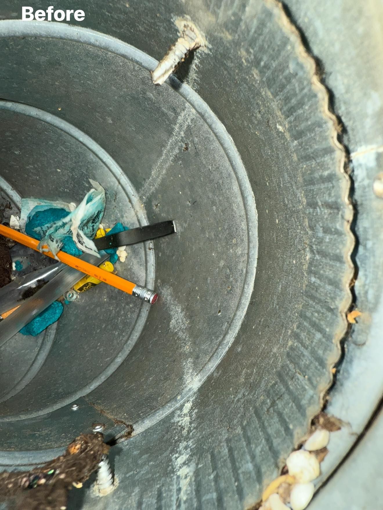 Close-up of a dirty, circular dryer vent with lint, debris, a pencil, and other trash inside.