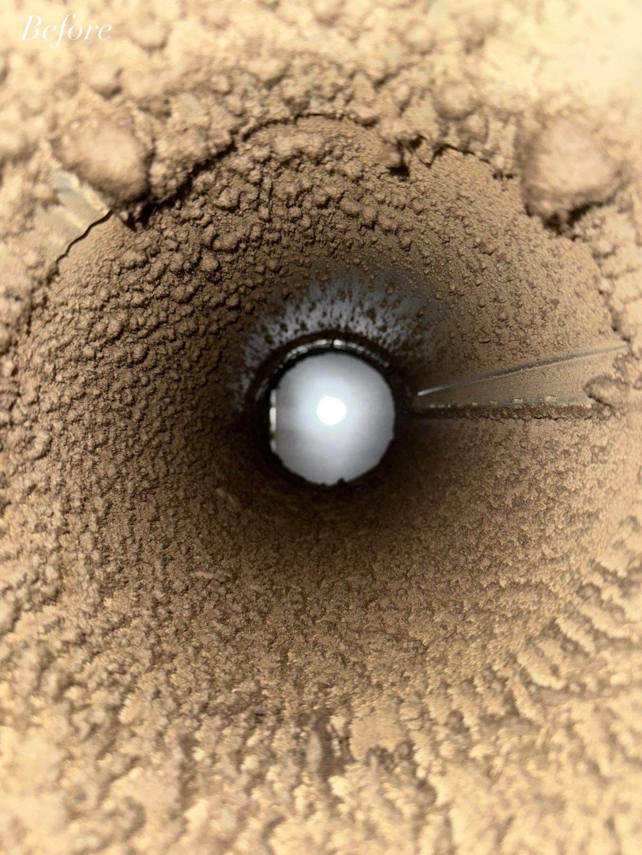 View inside a dirty, brown pipe. A white ball blocks the bottom.