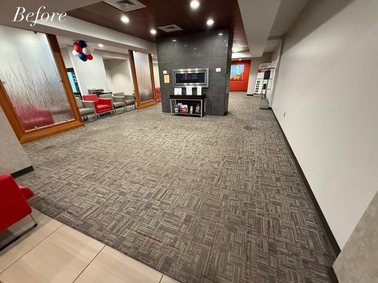 Lobby with patterned carpet, red and gray chairs, white and brown walls, and a TV.