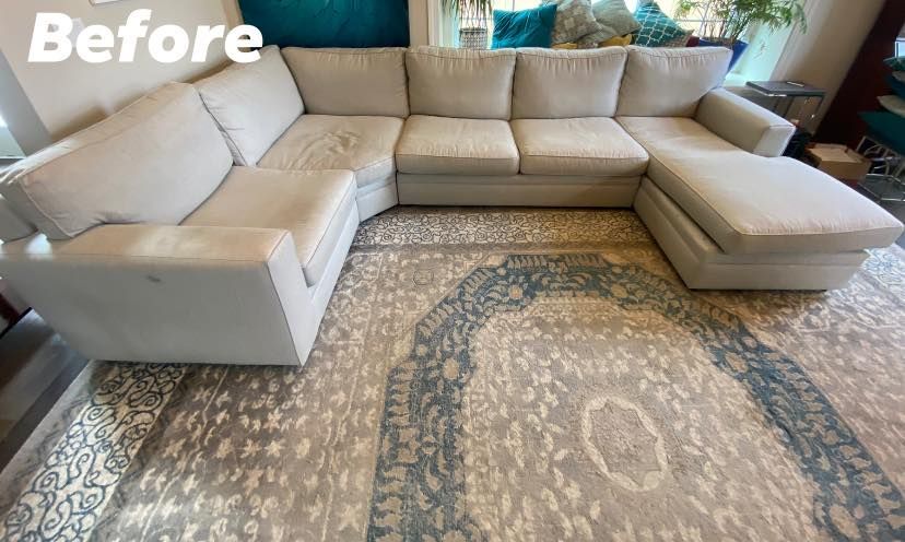 A light gray sectional sofa with stains on a patterned rug in a bright room.