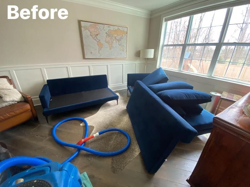 Blue sofa pieces and cleaning equipment in a room with a world map, a window, and beige walls.