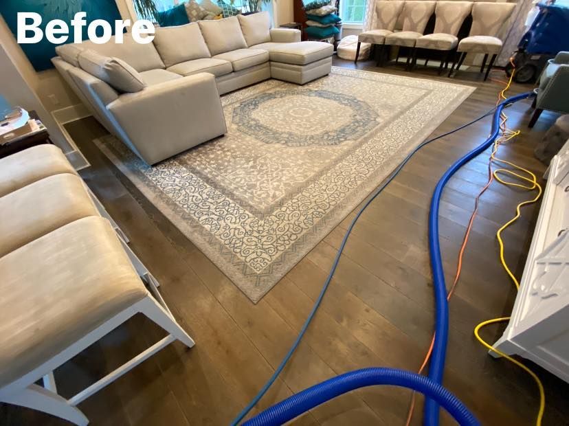Living room before rug cleaning: beige sectional sofa, large rug, vacuum hoses on wood floor.