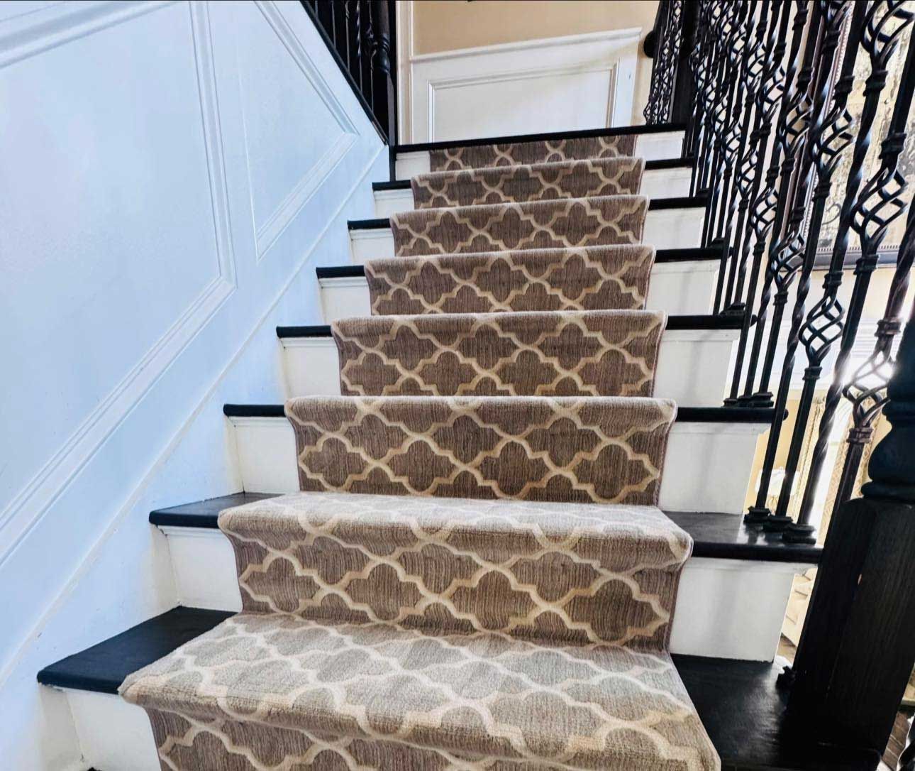 Staircase with brown patterned carpet runners, black and white steps, and black ornate railing.