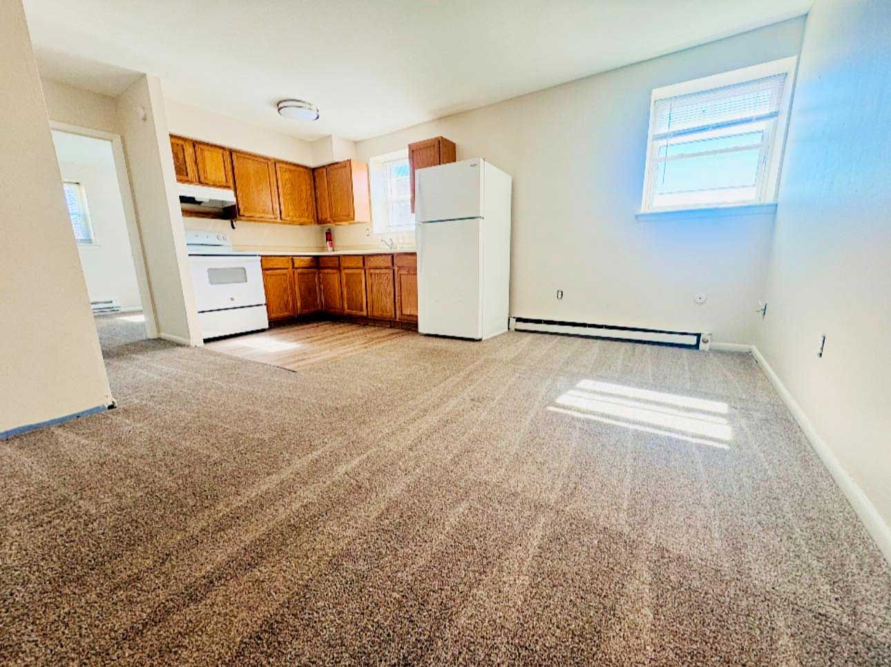 Kitchen with brown cabinets, white appliances, and tan carpet.