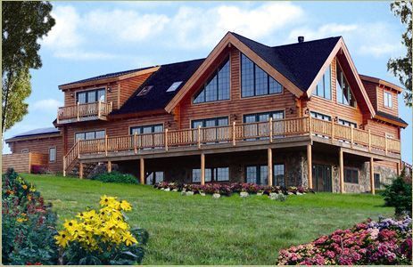 A large log home with a large deck sits on top of a lush green hillside