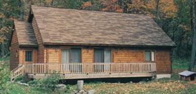 A small log cabin with a deck in the middle of a forest.