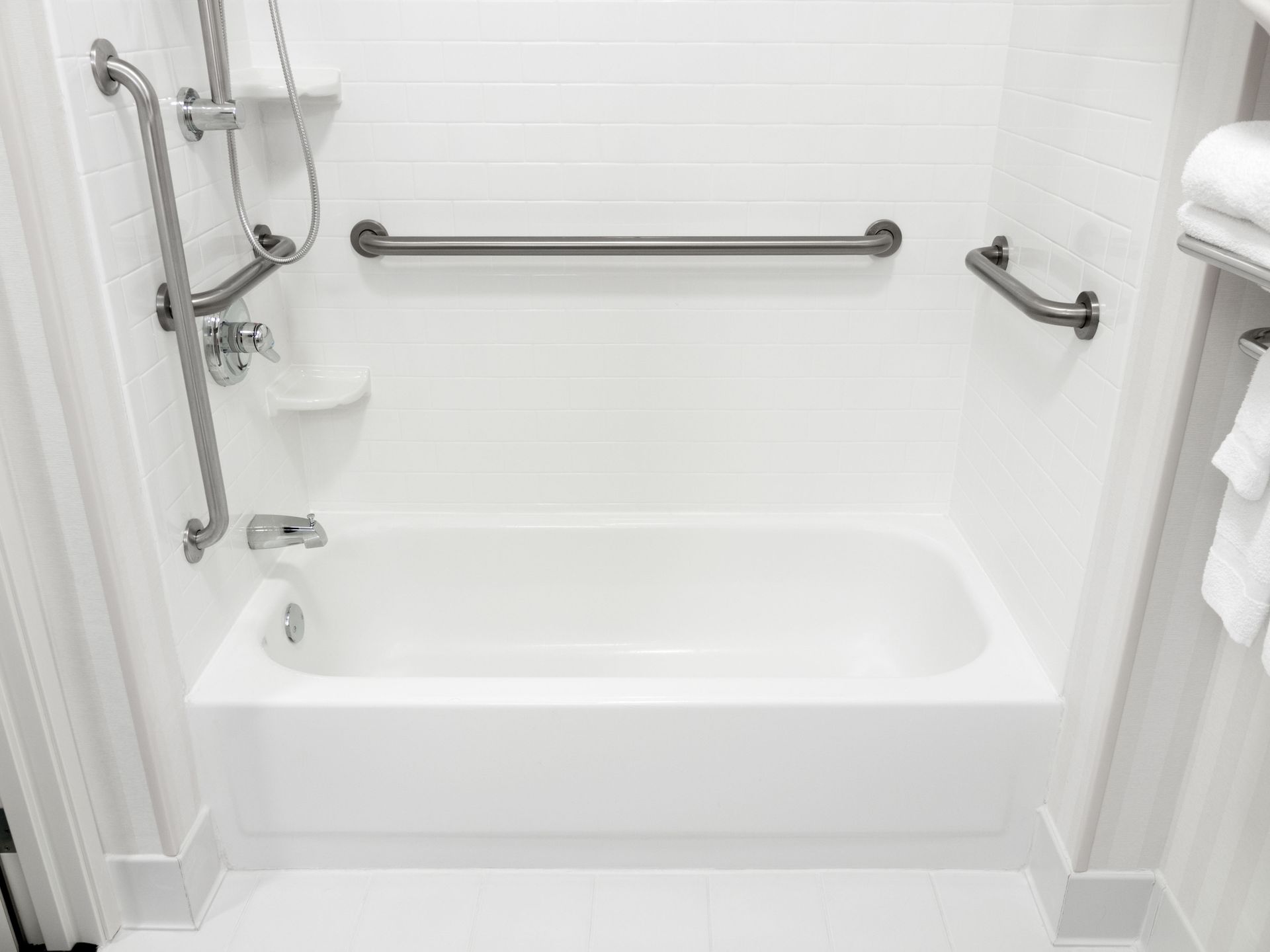 White accessible bathtub with grab bars; shower head, towels.