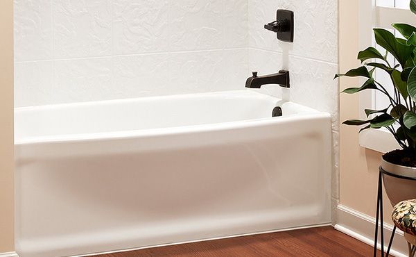 White bathtub with black faucet fixtures against white textured wall, hardwood floor, and a potted plant.