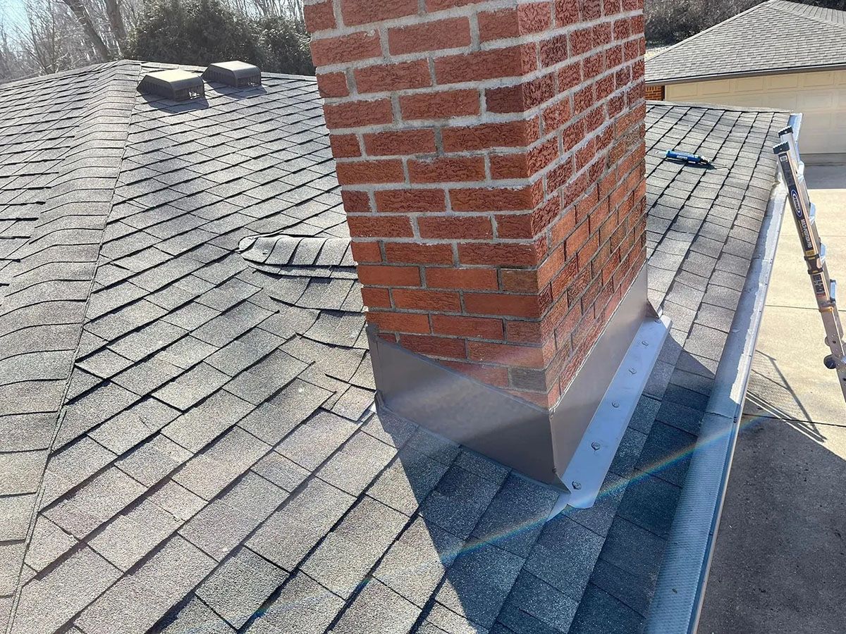 Brick chimney on a shingled roof with a metal flashing base