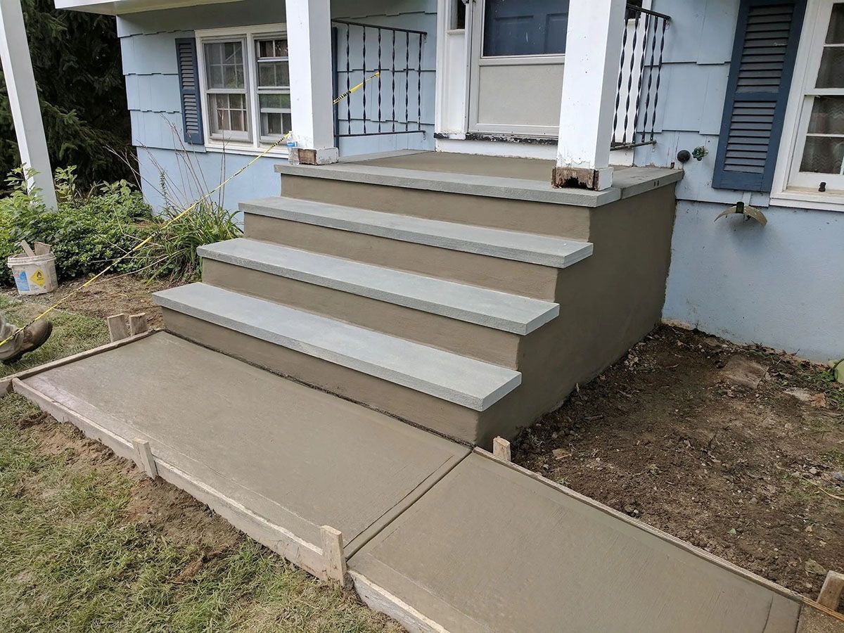 Concrete front steps and ramp leading to a house porch with white columns and windows