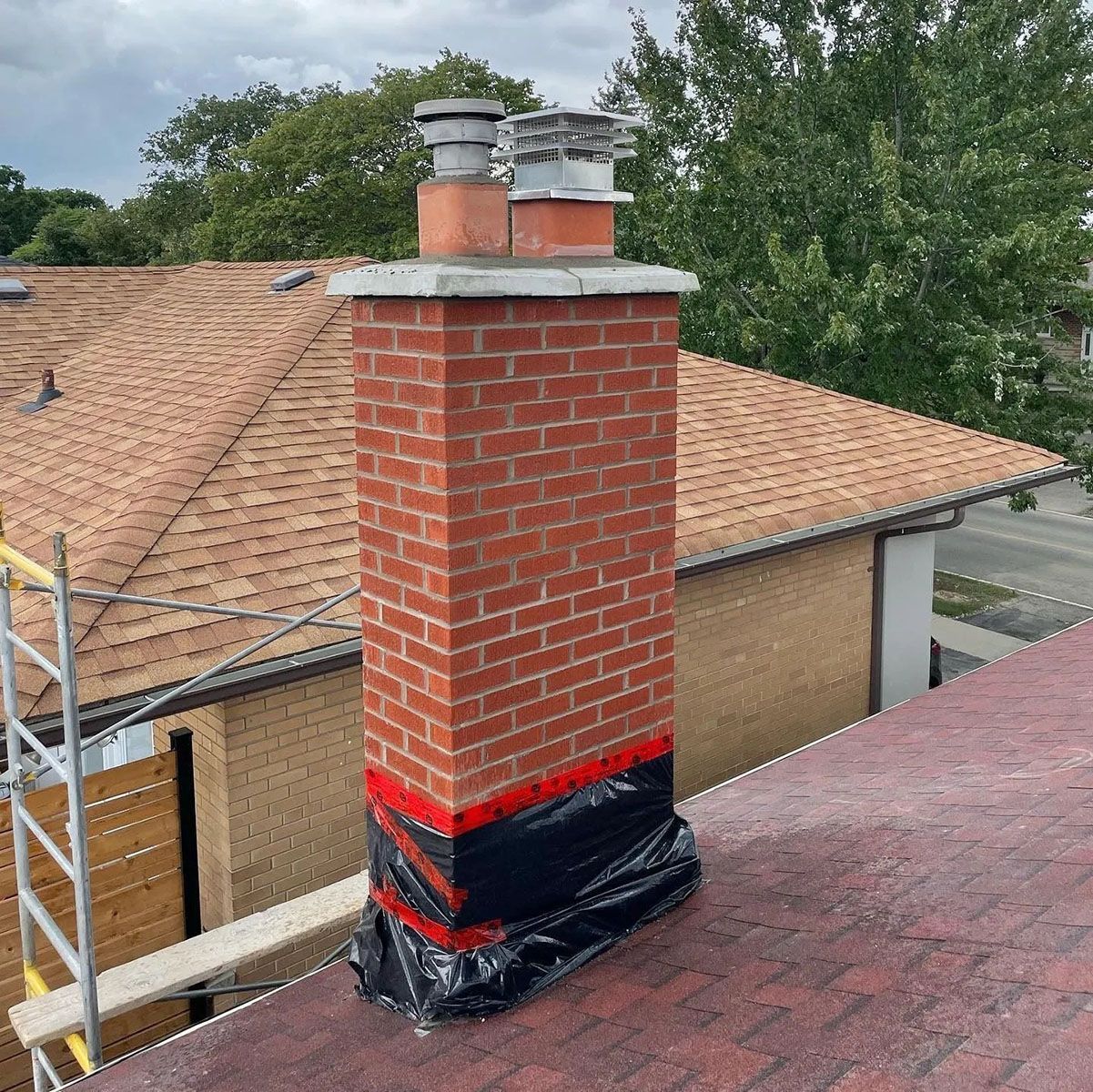 Brick chimney on a roof, wrapped at the base with black and red protective material