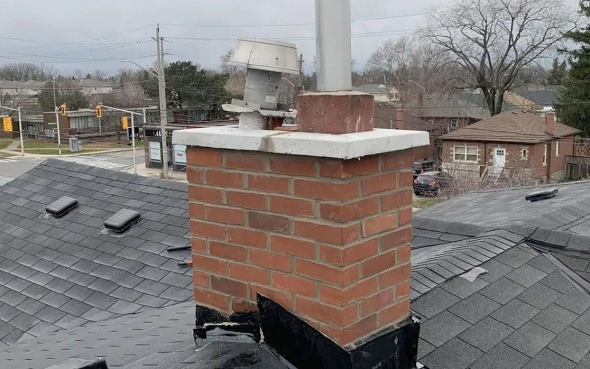 Brick chimney with white cap on a gray shingled rooftop in a residential neighborhood