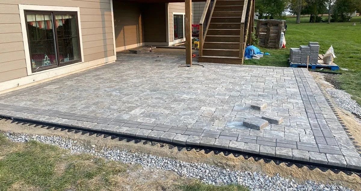 Stone patio beside a house with steps leading to a door and gravel border in a yard