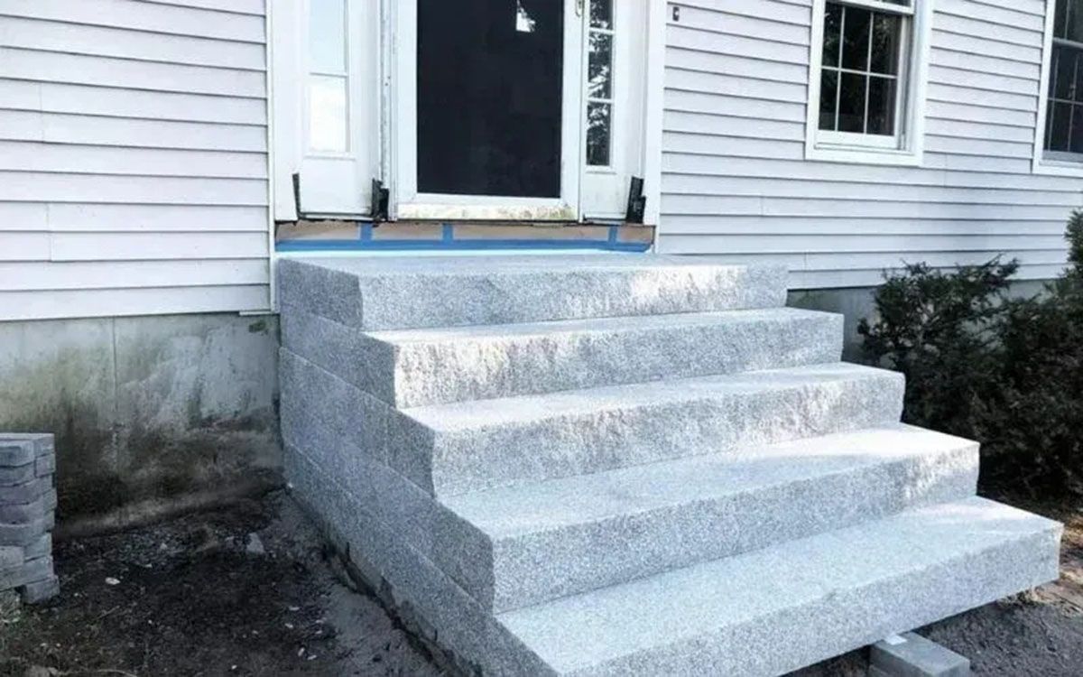 Concrete front steps leading to a house entry with a white door and gray siding