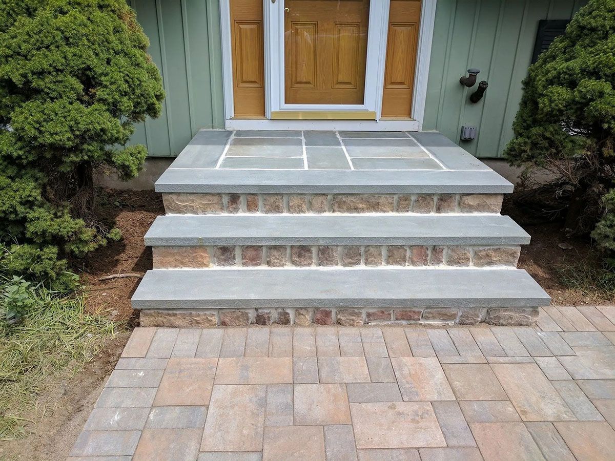 Front steps and walkway leading to a wooden front door with stone and brick trim