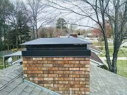 Brick chimney with dark metal cap on a residential roof, trees in the background.