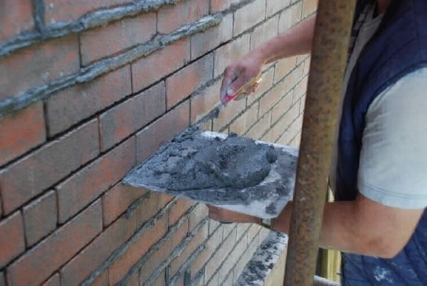 Person applying mortar to brick wall using a trowel and hawk.