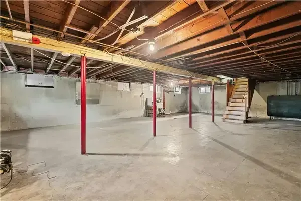 Unfinished basement with concrete floor, exposed wooden beams, red support posts, and stairs.