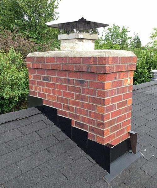 Brick chimney on a dark shingle roof with black flashing. A metal cap sits atop the chimney.