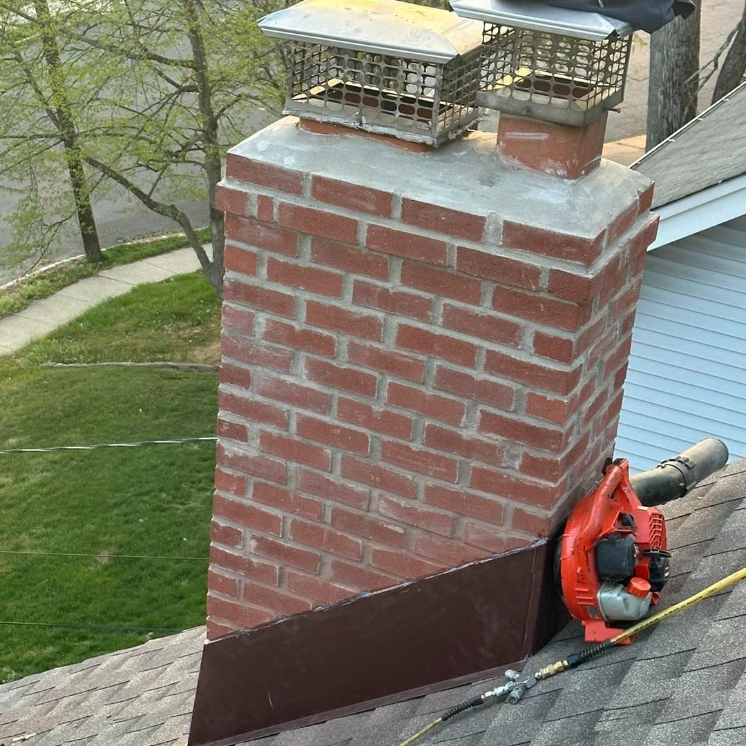 Brick chimney on a roof with a leaf blower and protective flashing.
