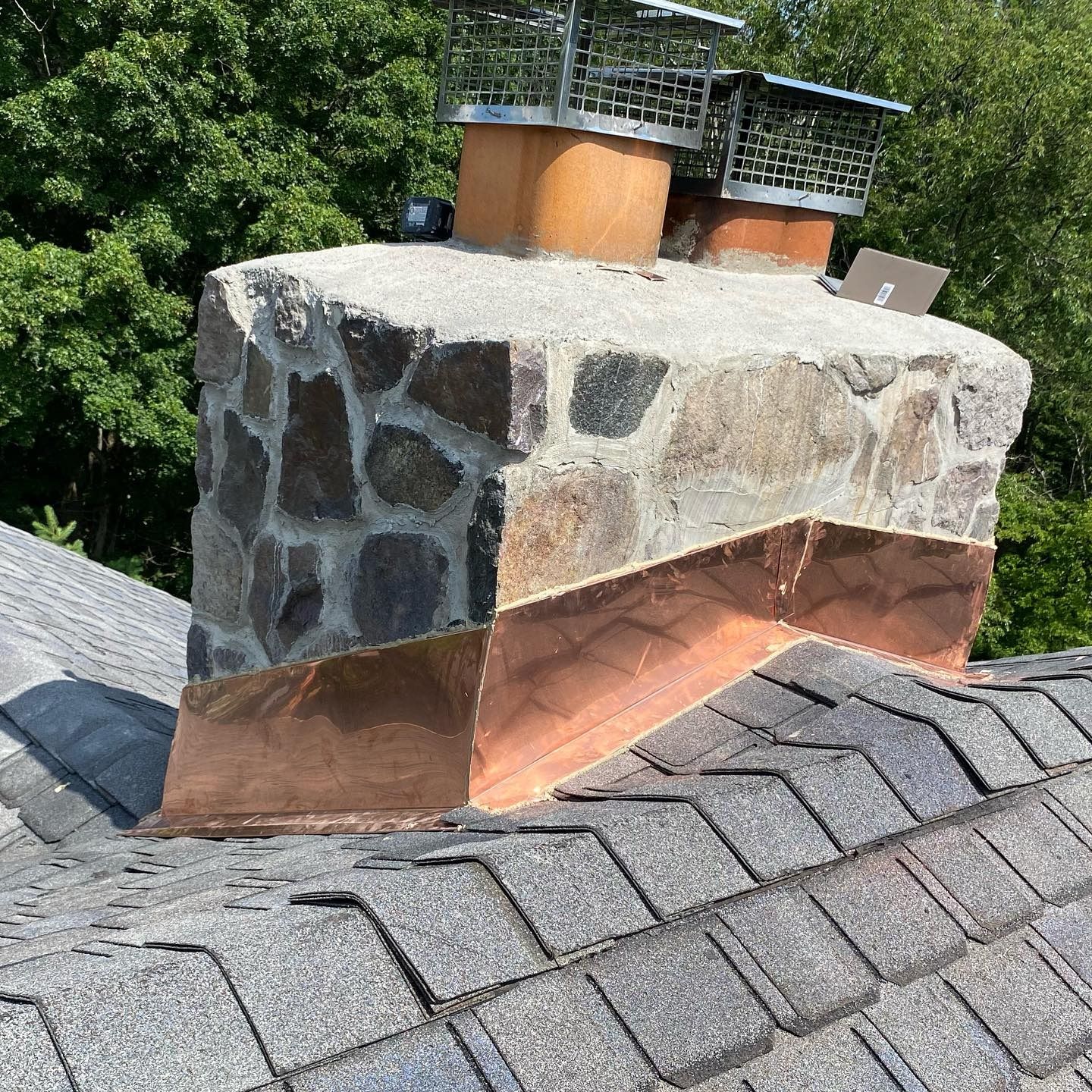 Chimney with copper flashing and stone facade on a gray shingle roof.