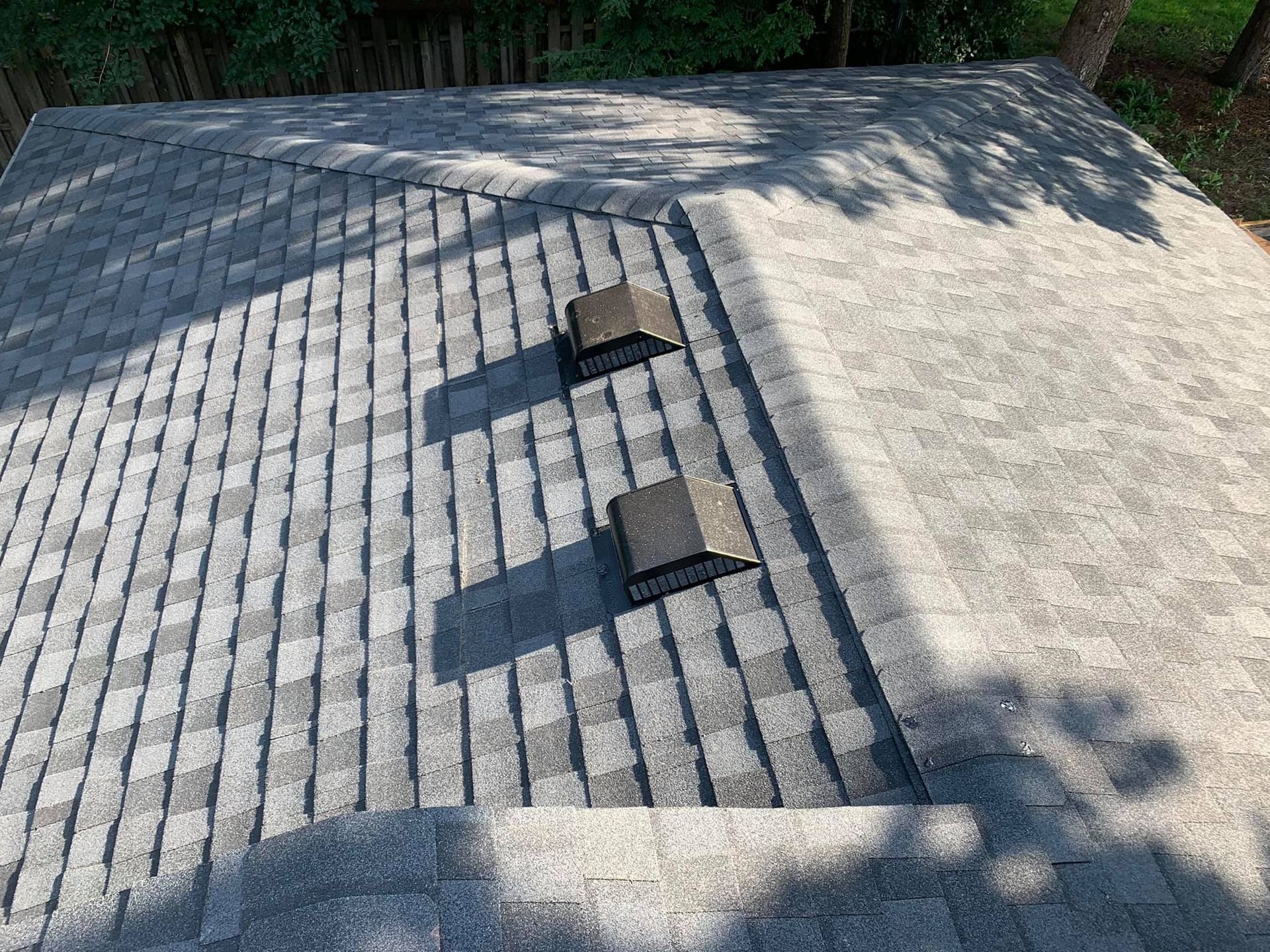 Gray asphalt shingle roof with two square vents, angled view.
