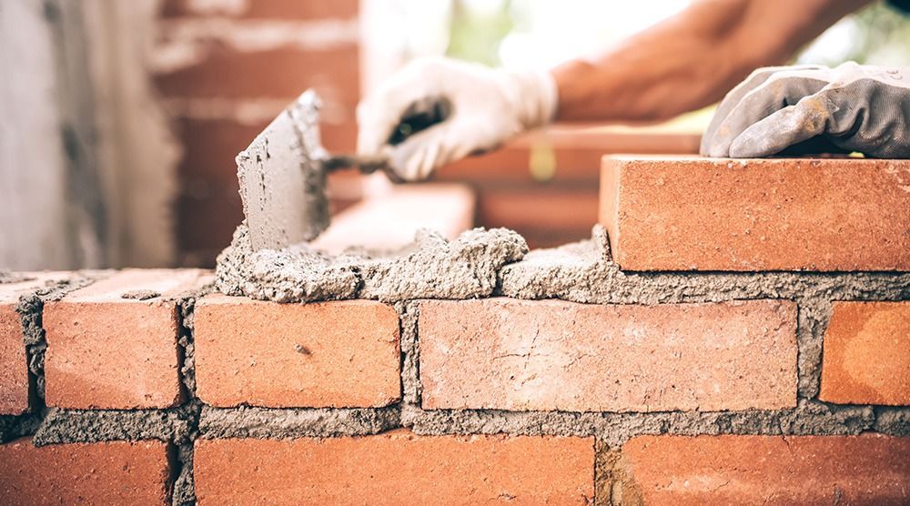 Close-up of gloved hands using a trowel to apply mortar on red bricks, constructing a wall.