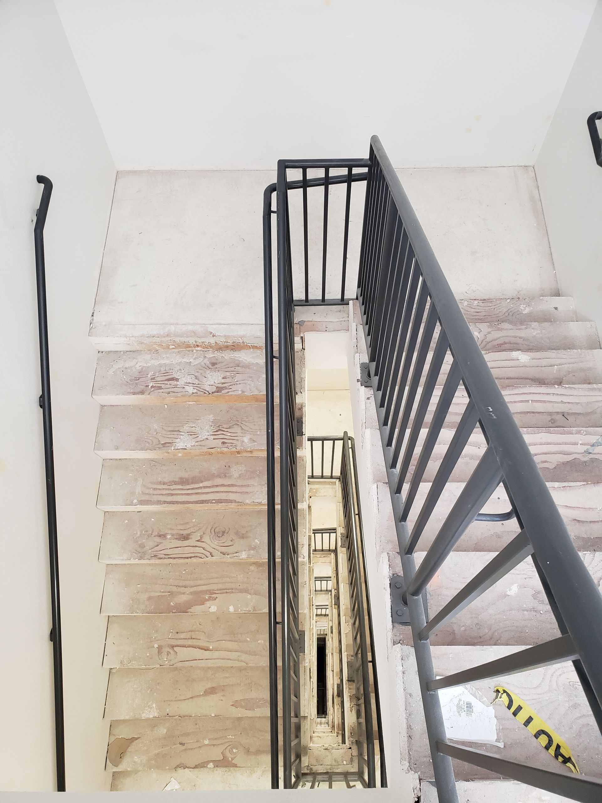 Stairwell viewed from above with metal railing on the right and long vertical descent.