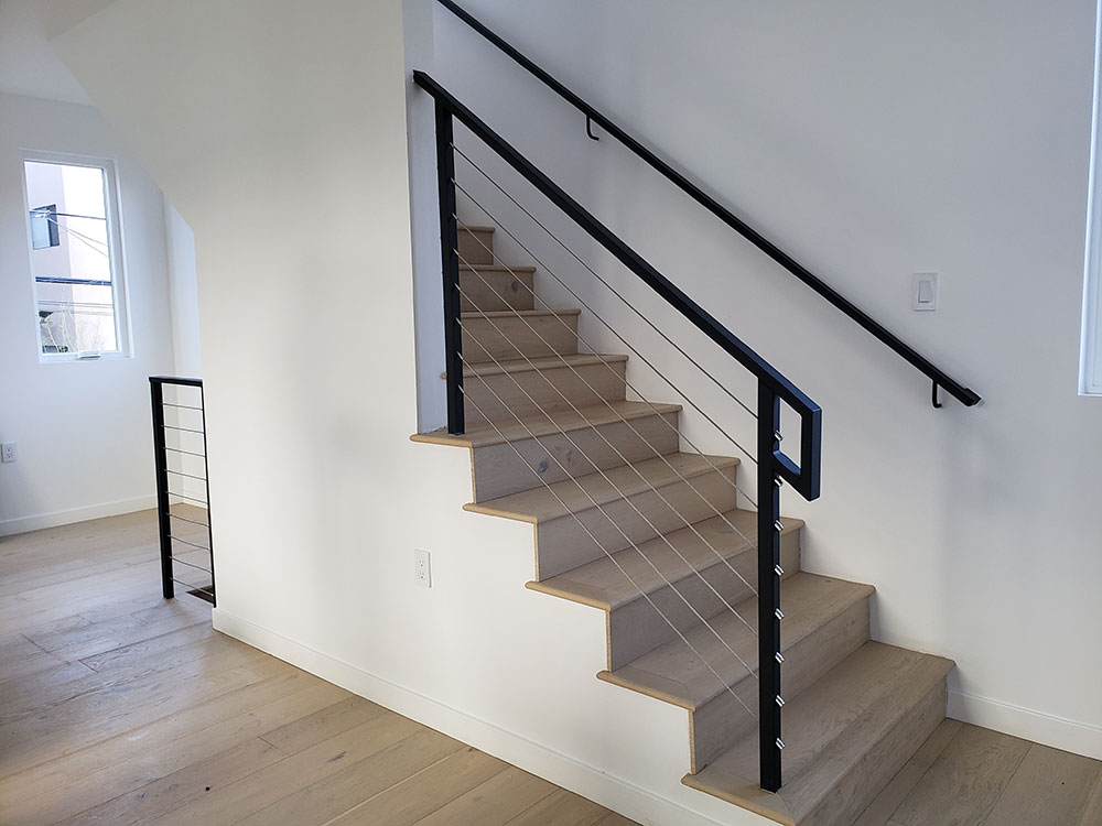 Staircase with light wood treads, white risers, black metal railing, and cable balustrade.