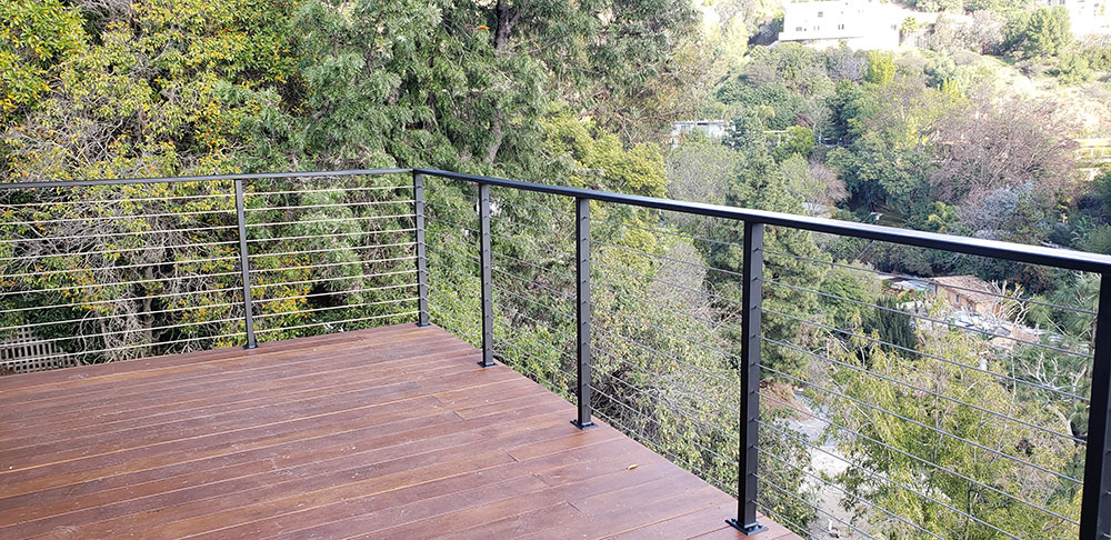 Deck with black railing overlooking lush green trees.