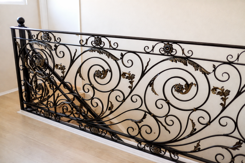 Ornate black wrought-iron stair railing with swirling scrollwork along a white stairwell