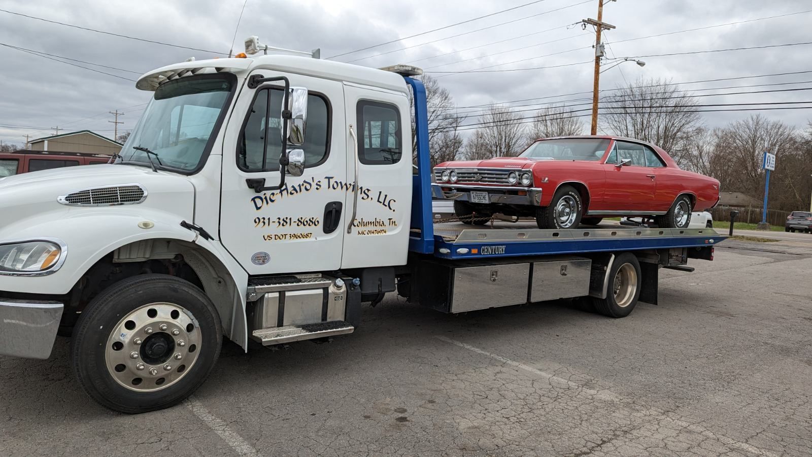 Tow truck carrying a red classic car on its flatbed in a parking lot