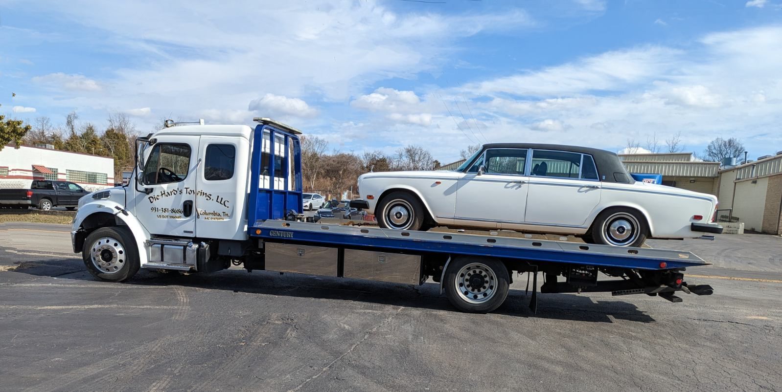 White coupe on a flatbed tow truck in a parking lot under a cloudy sky
