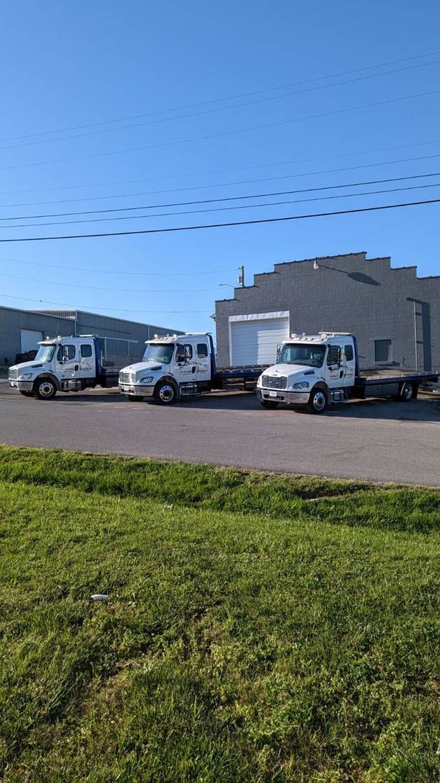 White trucks parked outside a light-colored industrial building on a sunny day, with green grass in front