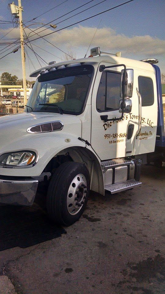 White tow truck parked outdoors with open passenger door and Hebrew text on the side