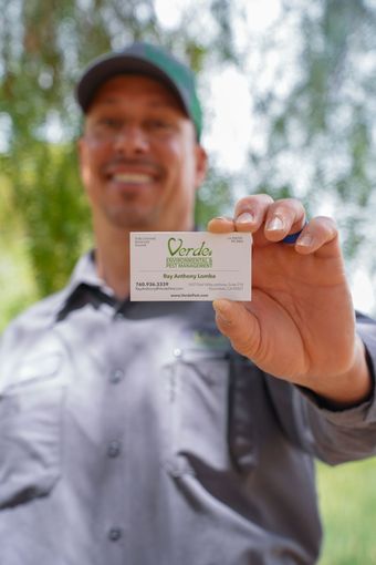 Man holding out a business card outdoors, with blurred trees in the background.