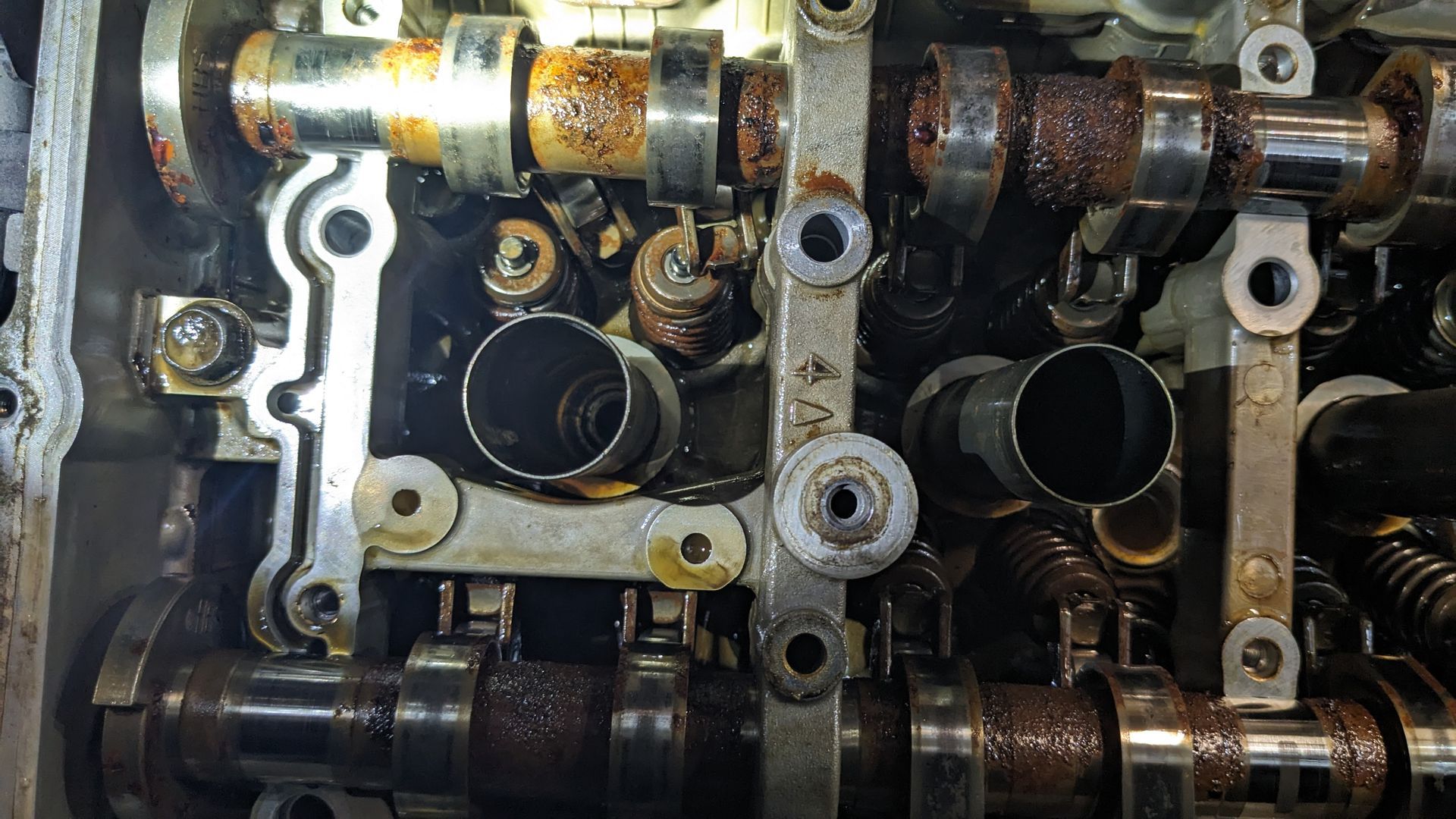 Close-up of a car engine cylinder head with camshafts, valves, and oil-stained metal parts