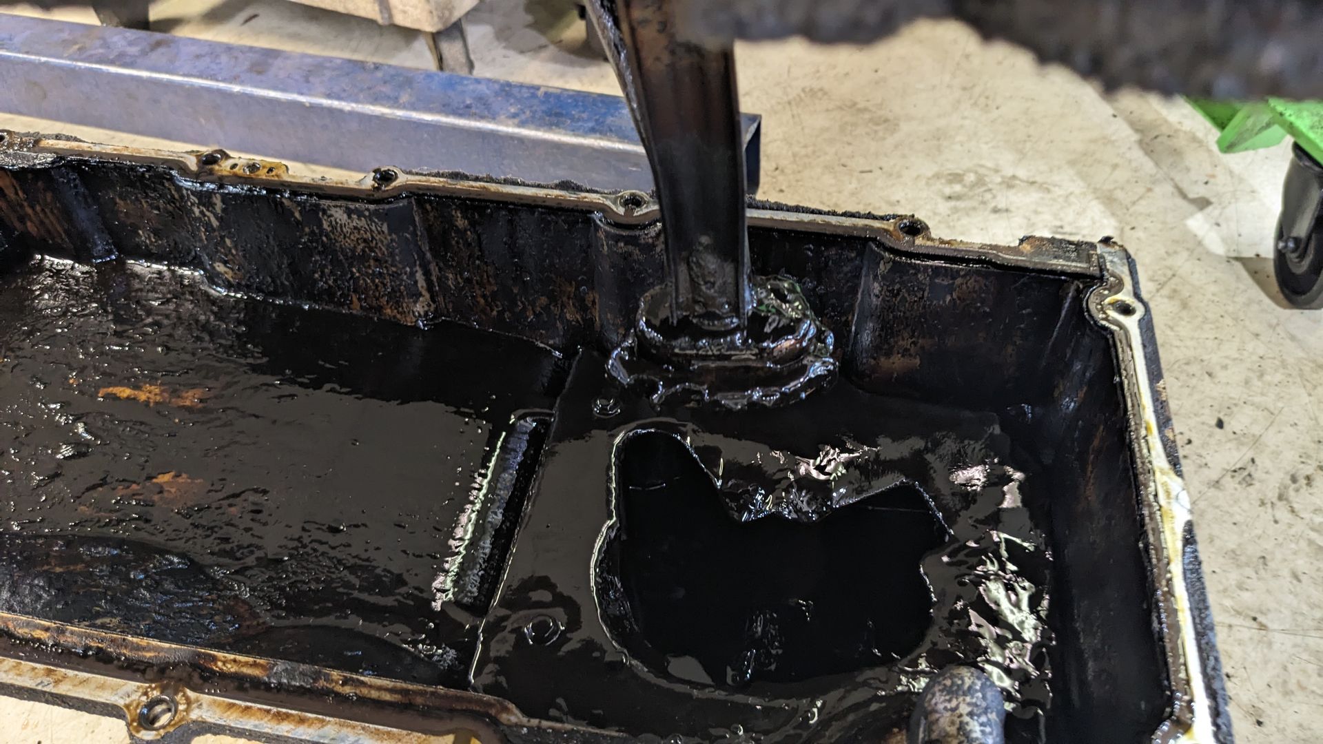 Black liquid spilled inside a container, with a tool stirring or pouring into it.