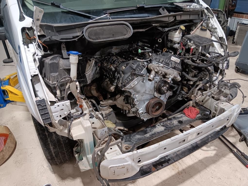 Severely damaged white vehicle with exposed engine in a collision repair shop