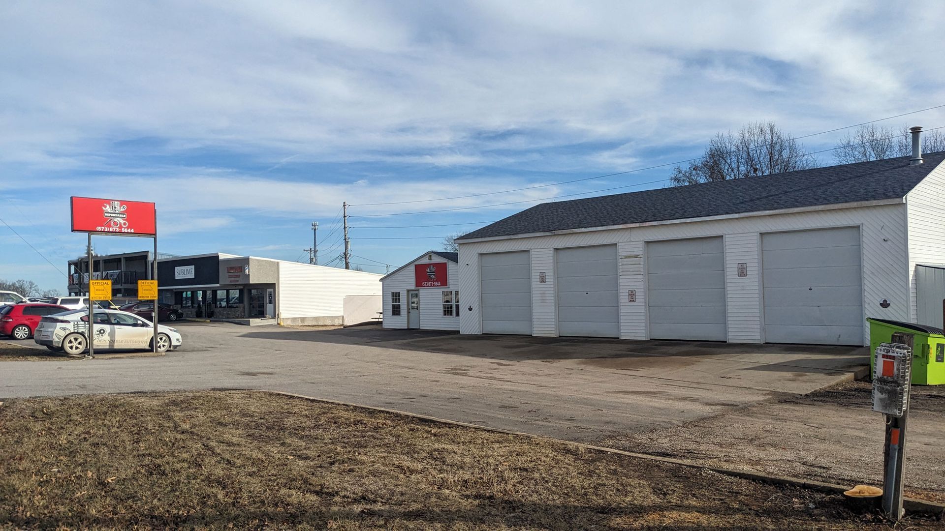 Industrial yard with white storage buildings, a red truck, and construction equipment under a cloudy sky
