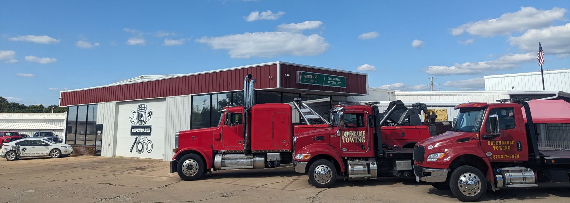Red tow trucks parked beside a white building under a blue sky