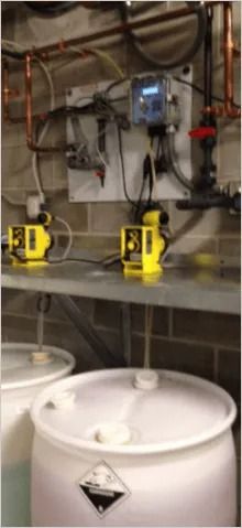 Industrial equipment: yellow pumps, white barrels, metal piping, control panel.