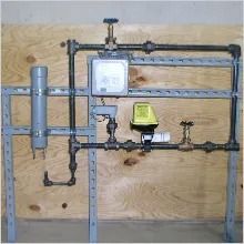 Plumbing system model with pipes, valves, and a control box, mounted on a metal frame.