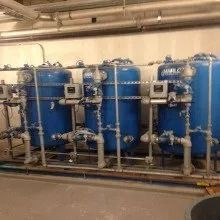 Blue industrial water filtration system with piping and gauges.