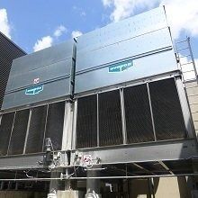 Two large metal cooling towers on a building roof against a blue sky.